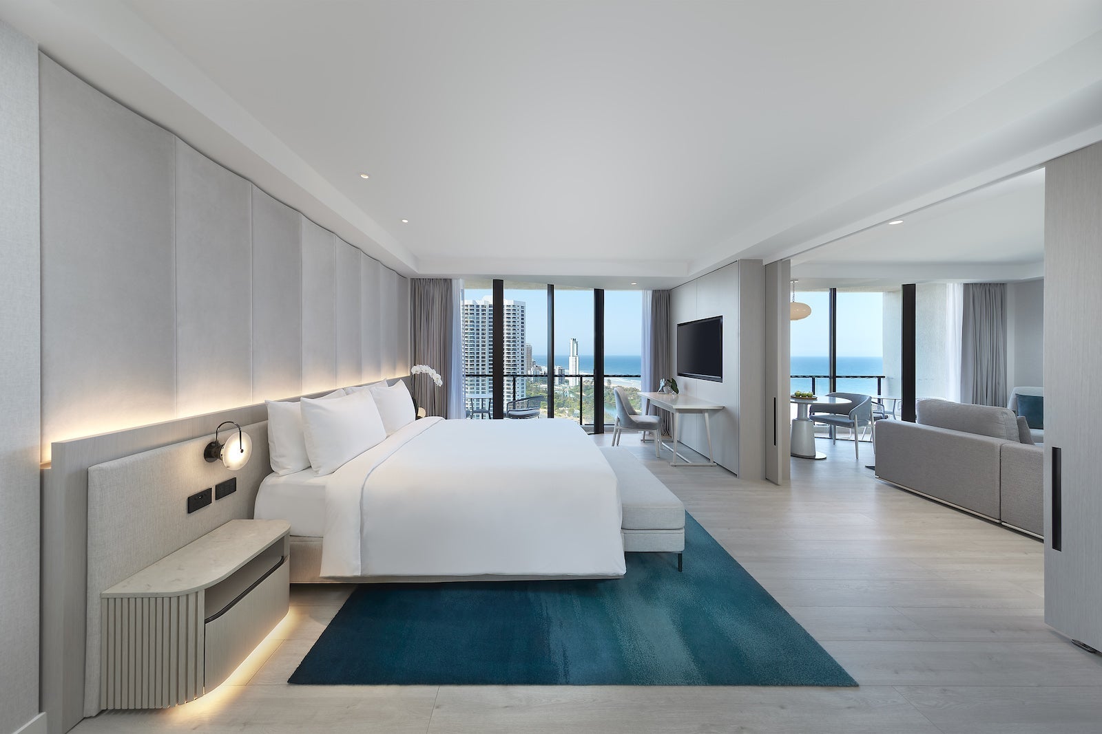 large modern hotel room with bed, blue rug and airy feel with large floor-to-ceiling windows
