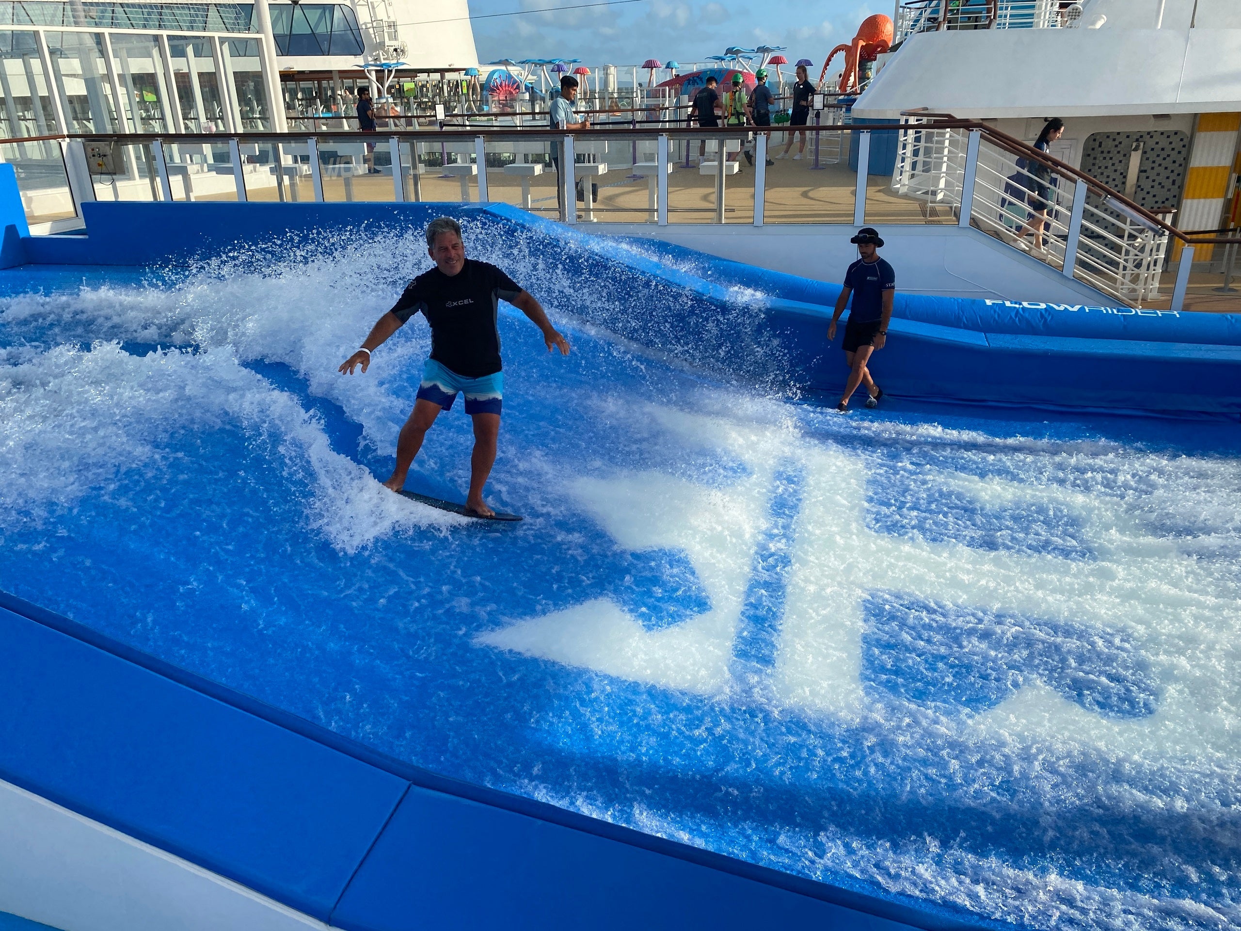 A main in swim trunks and a rash guard surfing on the FlowRider on a Royal Caribbean cruise ship
