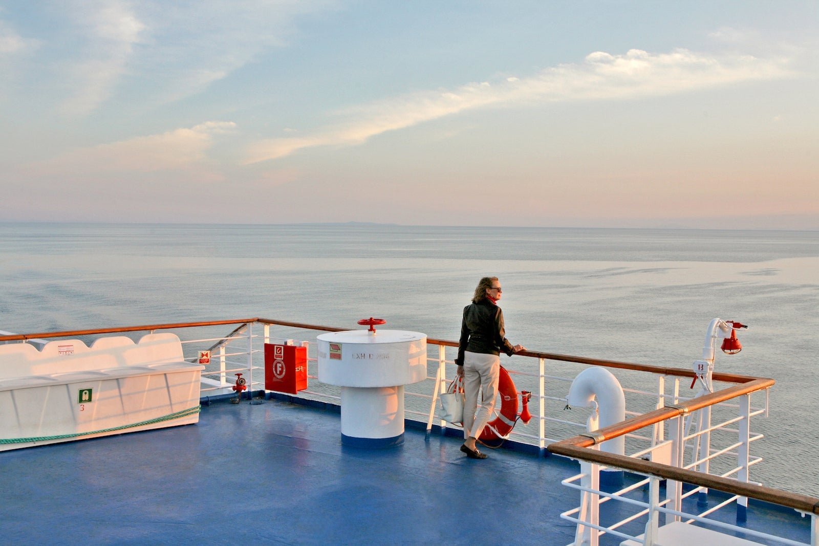 Person standing against the railing on the outer deck of a cruise ship looking at the ocean