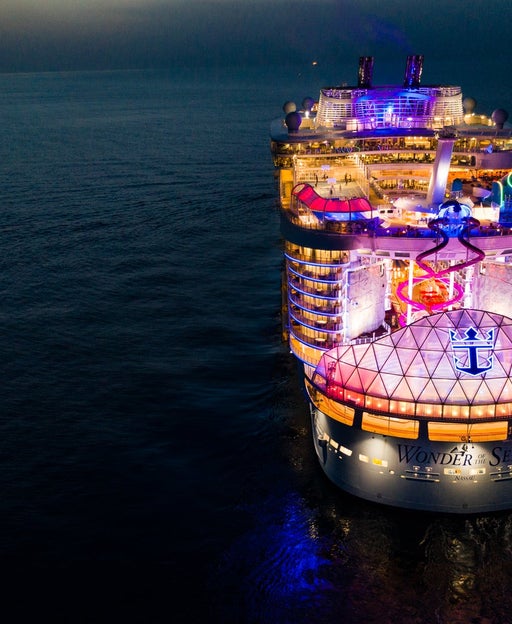 Aerial image of Royal Caribbean's Wonder of the Seas lit up with colored lights surrounded by the dark ocean at nighttime