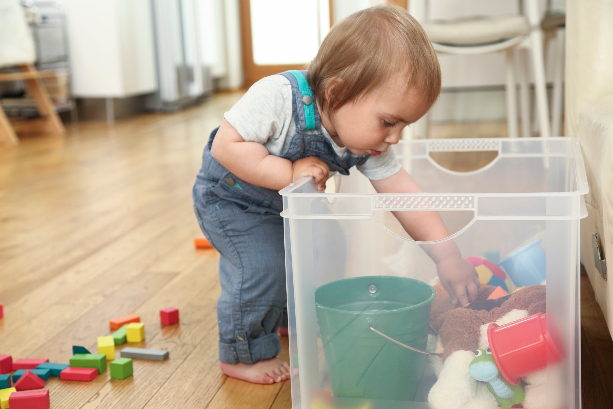 Toddler reaches for toys in clear bin
