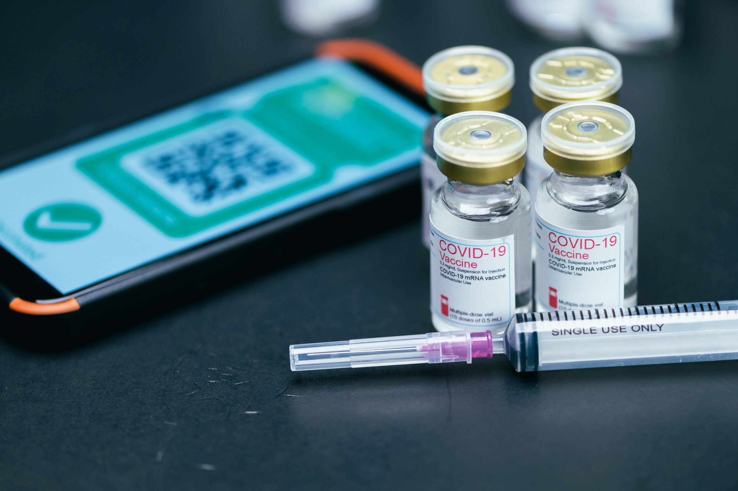 the close-up image of the COVID-19 bottle and vaccinated QR code on smartphone with the black backdrop