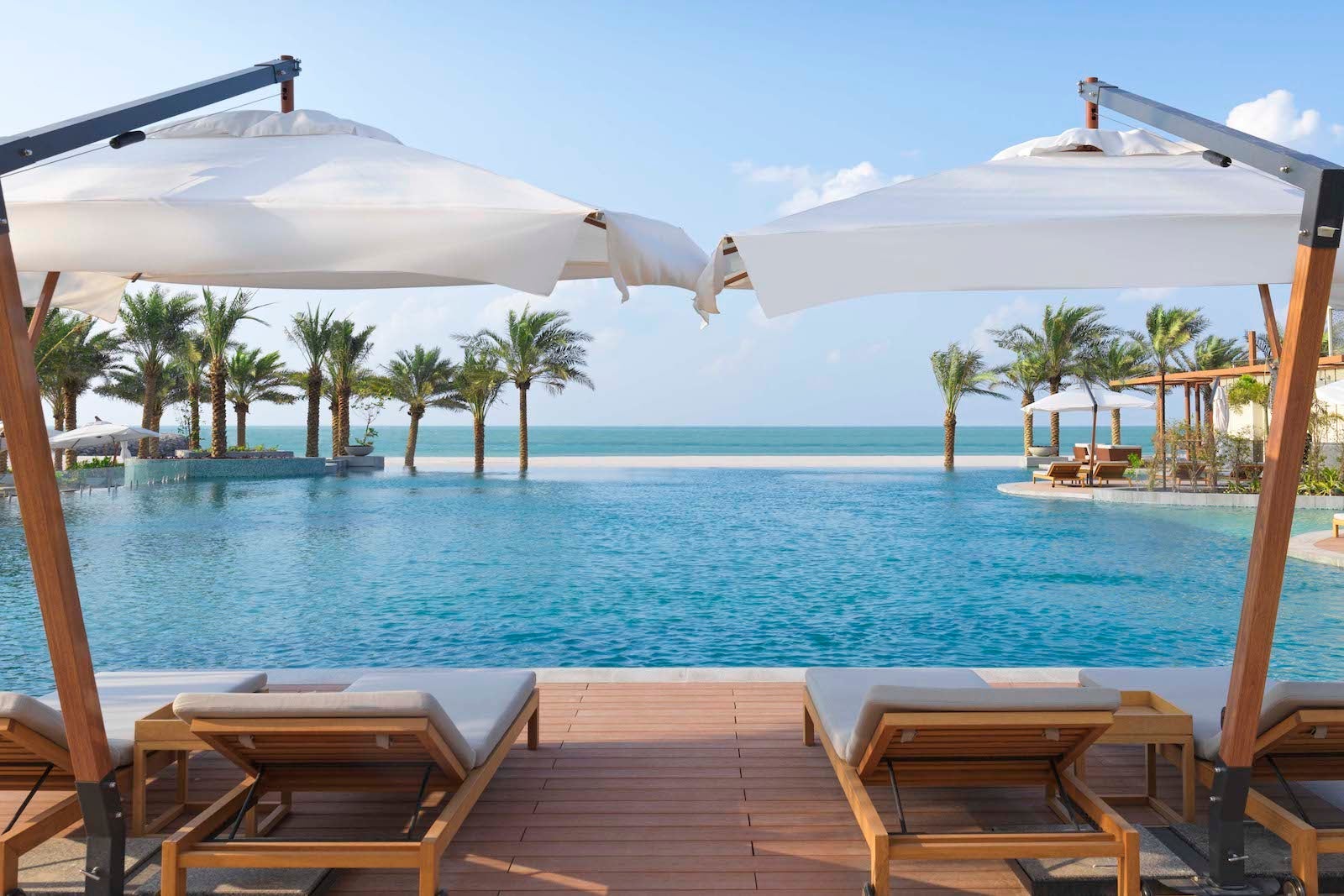 large umbrellas over lounge chairs in front pool by beach