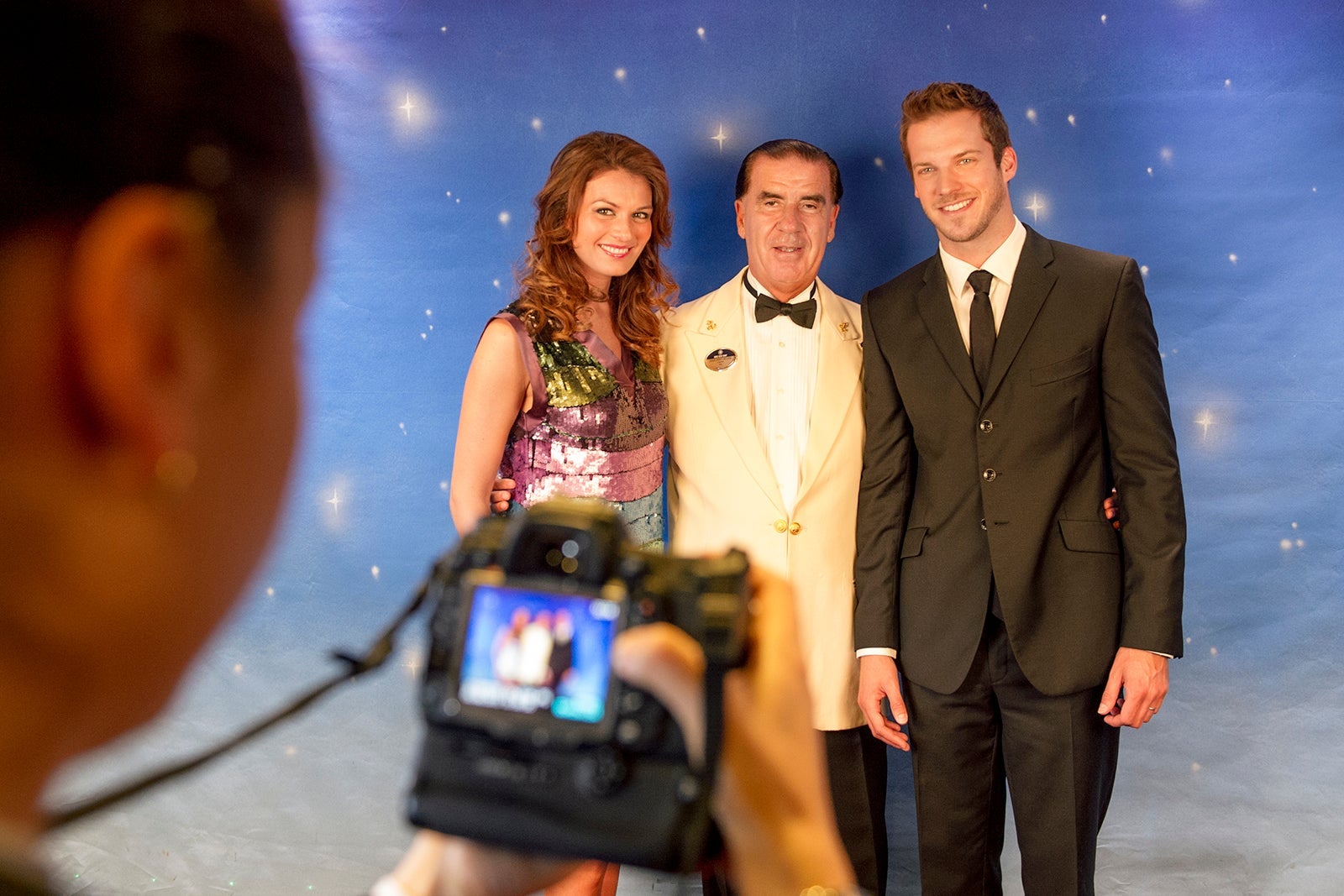 Couple in formalwear posing for a photo with cruise ship crew member in white tux