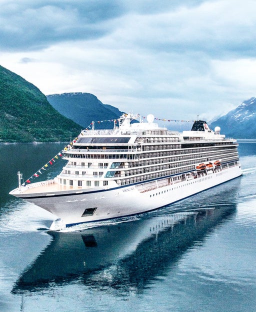 A white cruise ship sailing through a fjord with mountains and a cloudy sky in the background