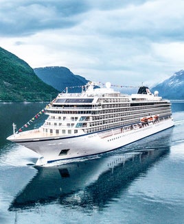 A white cruise ship sailing through a fjord with mountains and a cloudy sky in the background