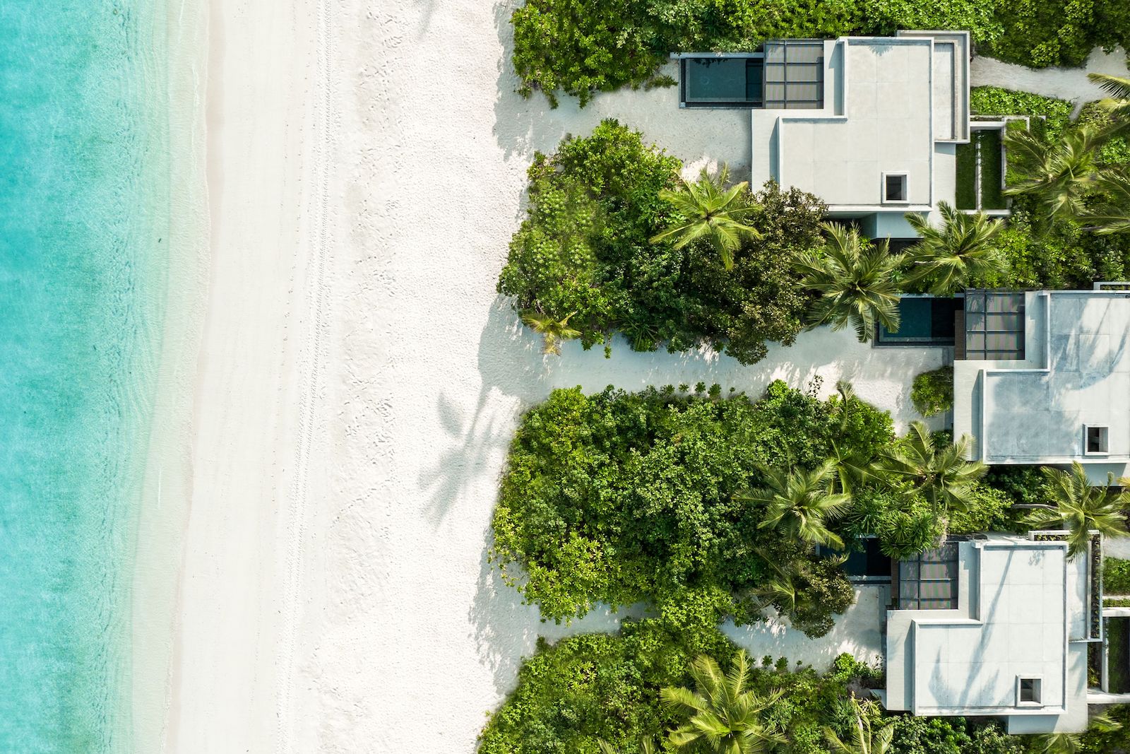 aerial view looking down on hotel villas, white beach and turquoise blue ocean water