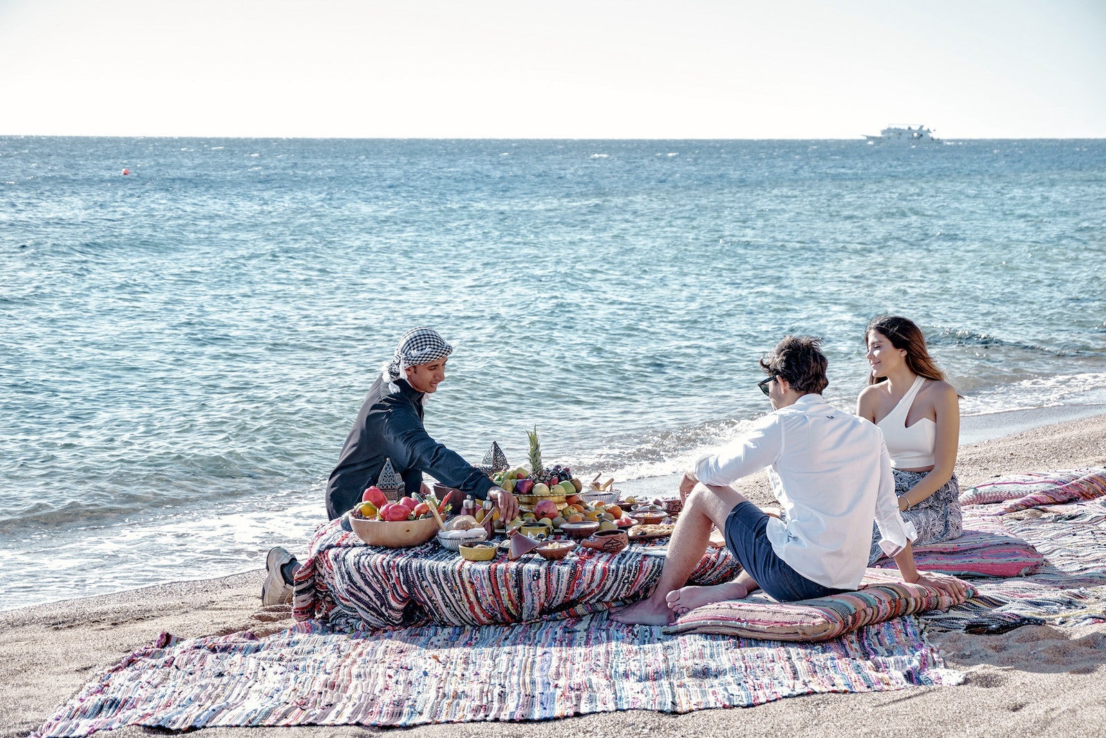 bedouin man and couple sitting on beach eating food