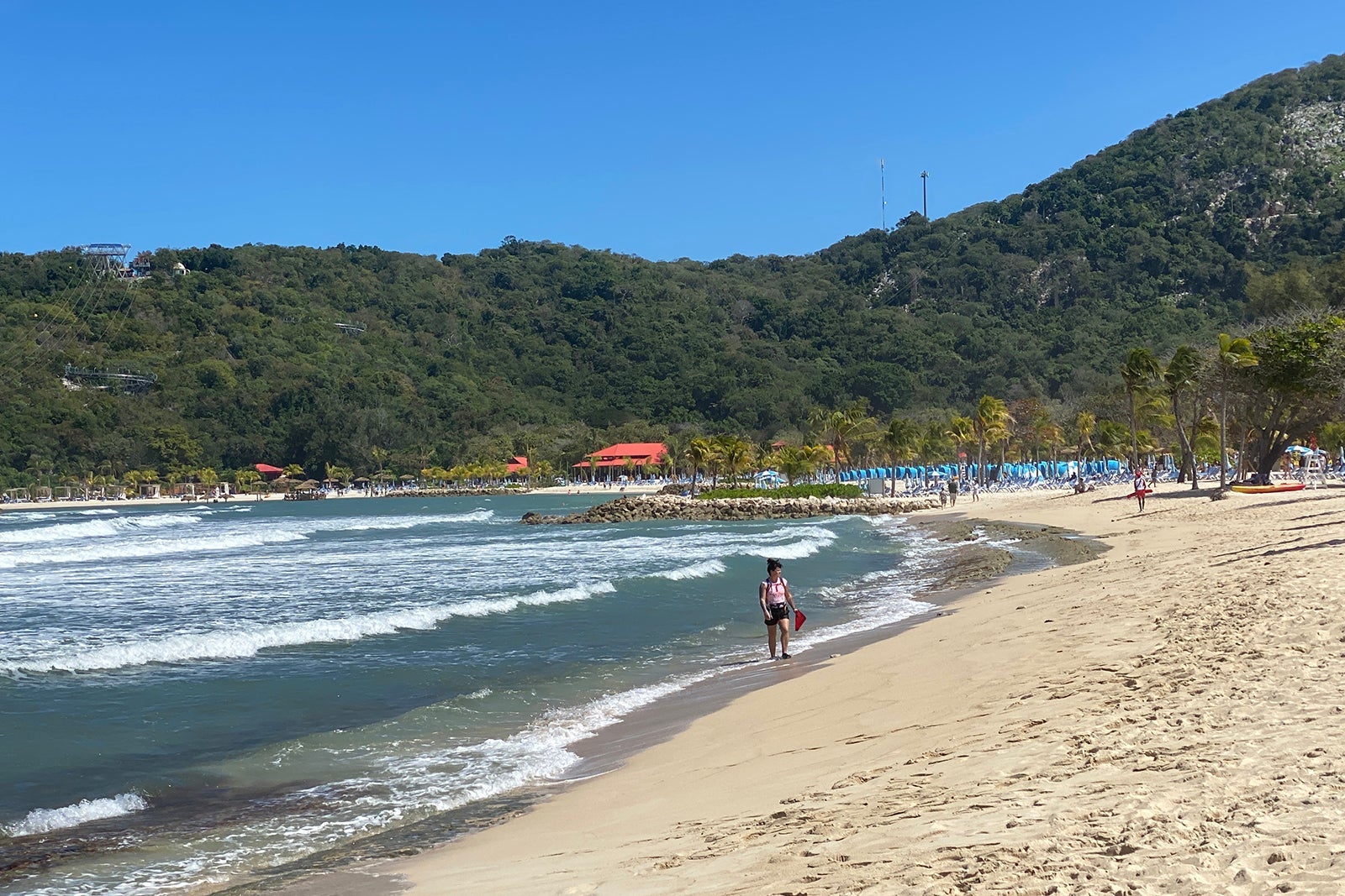 Woman walking on beach with green mountains behind her