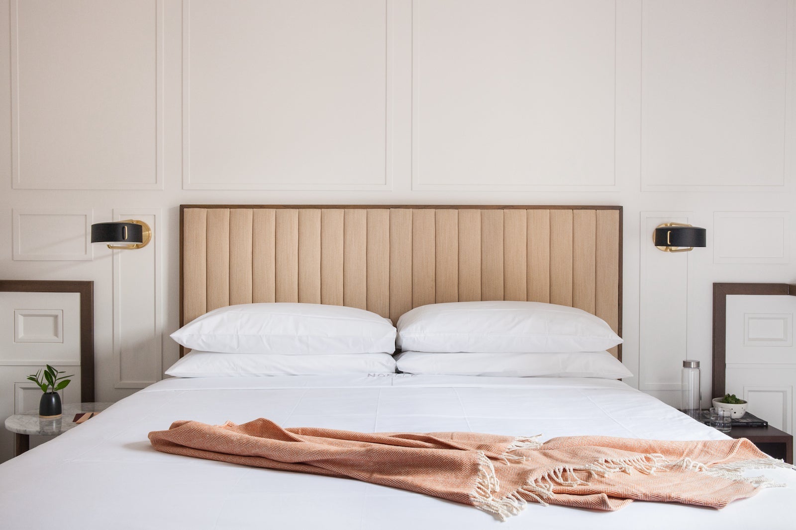 clean, white bed against white wall with tan, tufted headboard