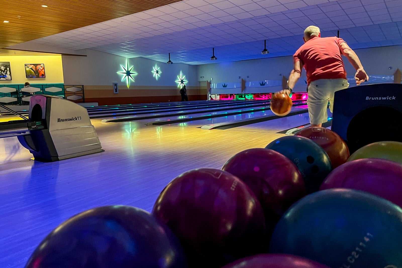 A man is seen bowling with a row of bowling balls in the foreground.