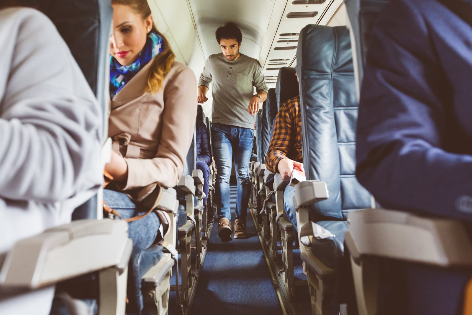 a passenger walks down the aisle of a crowded airplane