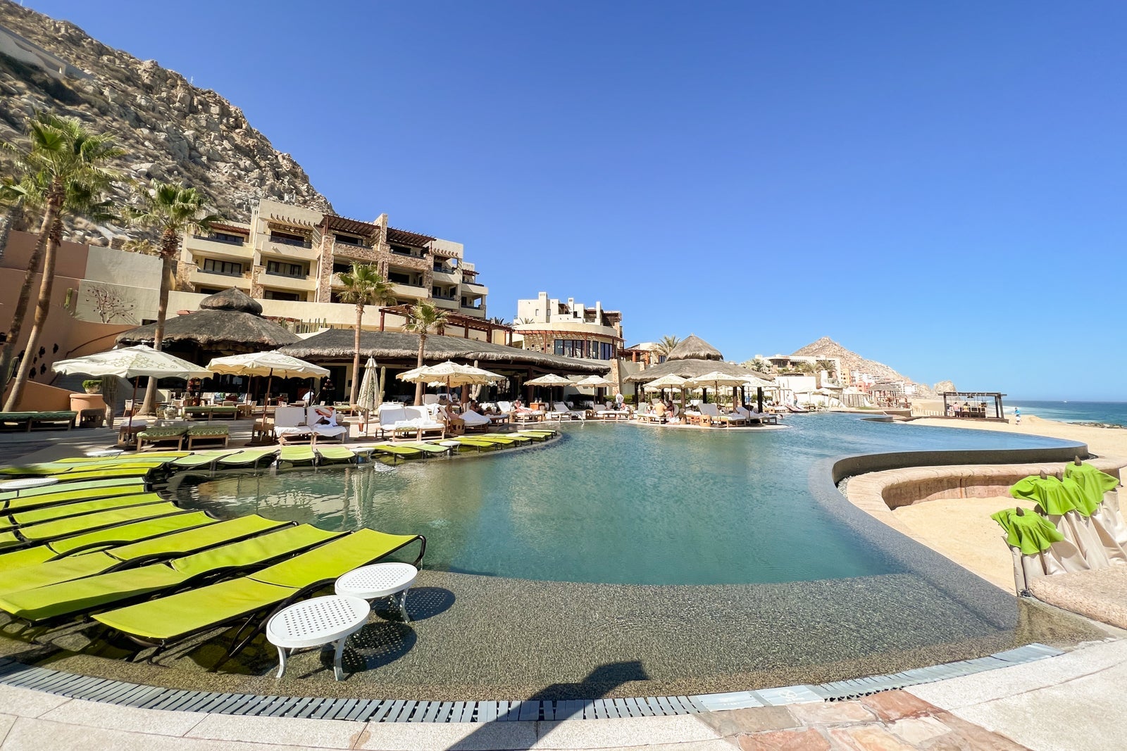 lounge chairs flank an infinity pool while a hotel built into a cliffside is visible in the background, overlooking the ocean