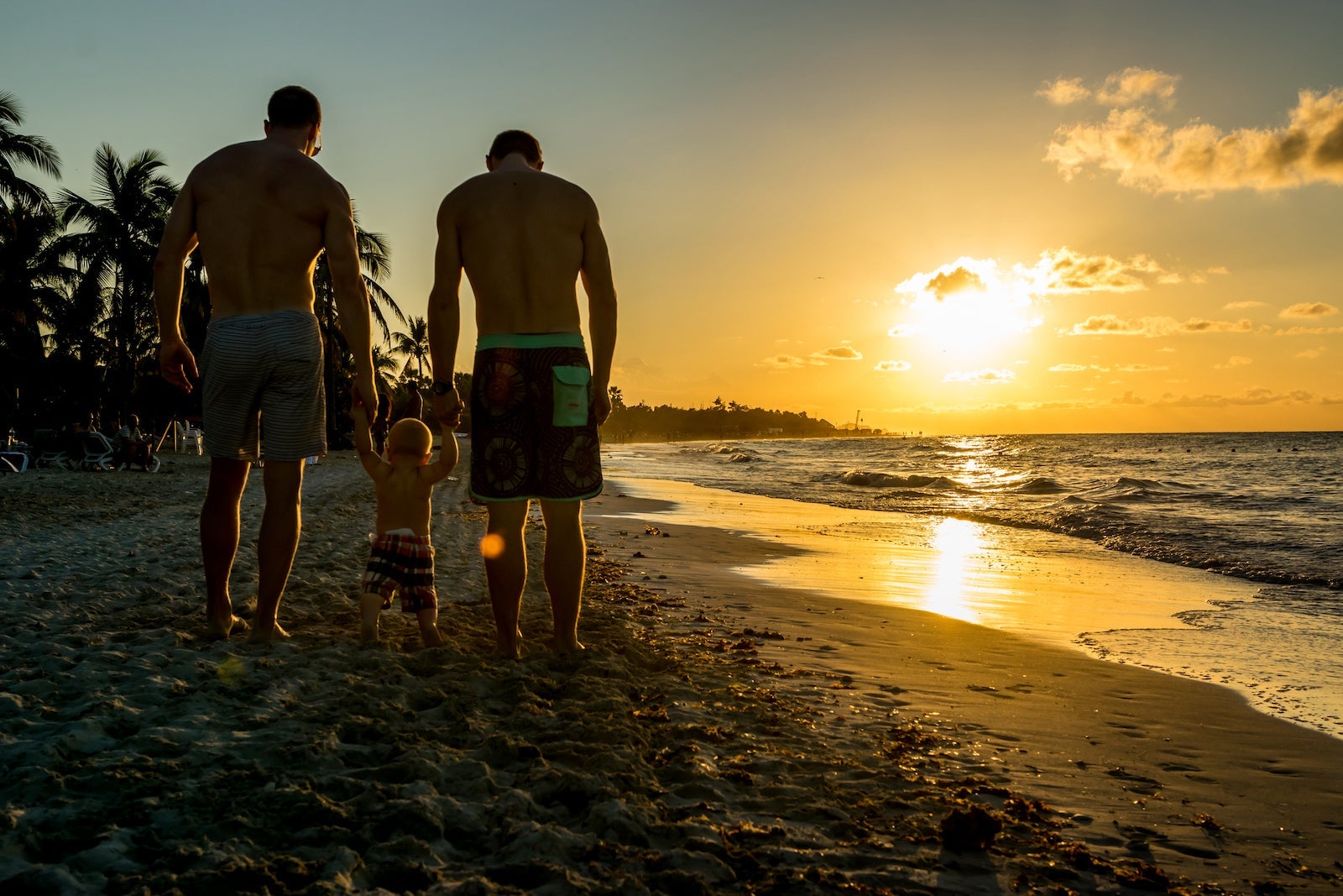 A couple walks with an infant between them, all holding hands