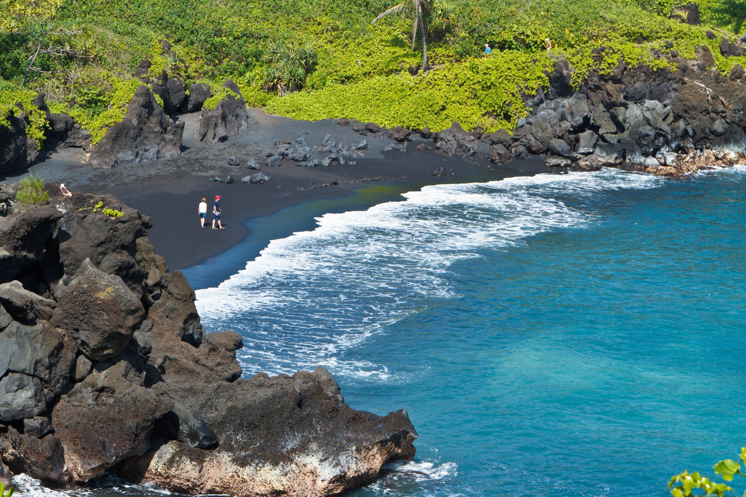 Two people standing on black sand beach at Waianapanapa State Park in Hana, Maui