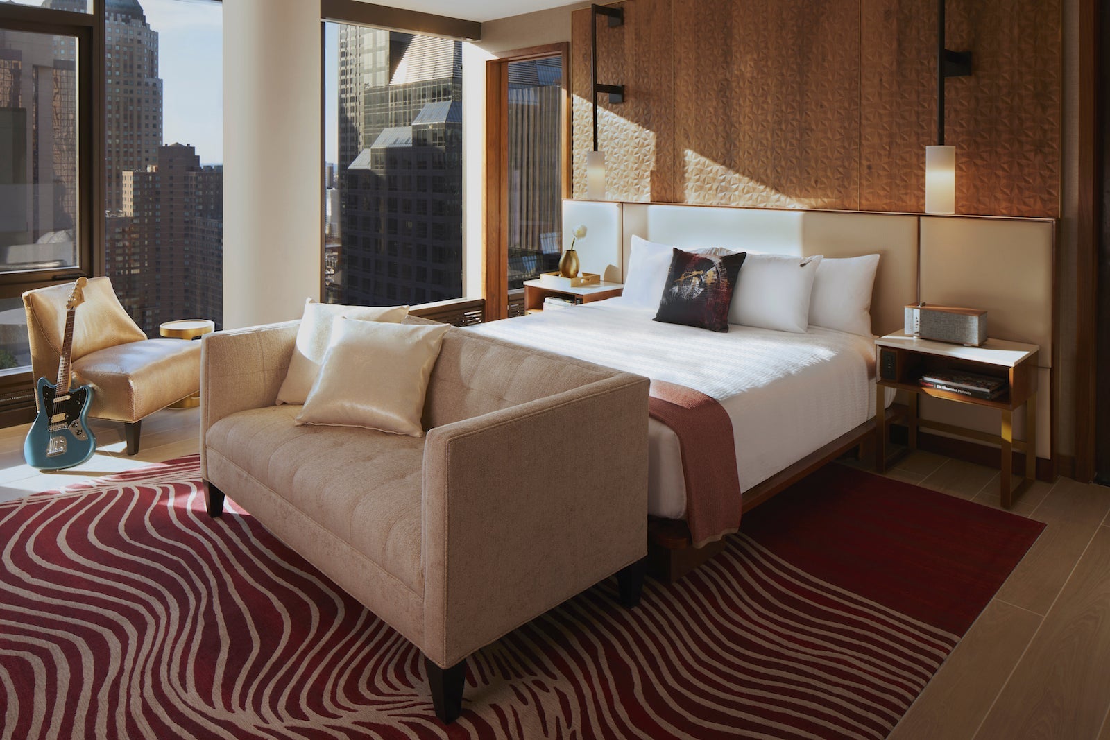 hotel suite with white linens, couch in front of bed and chair near window with electric guitar