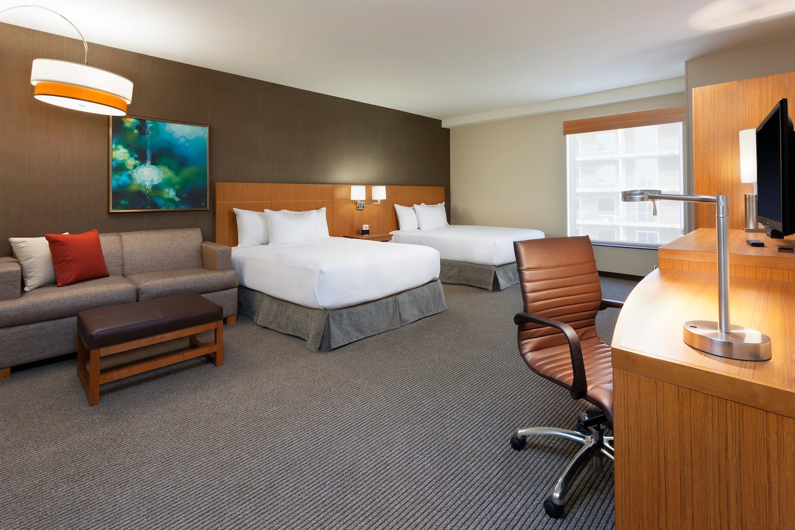 large hotel room with grey floors, couch, desk and two beds