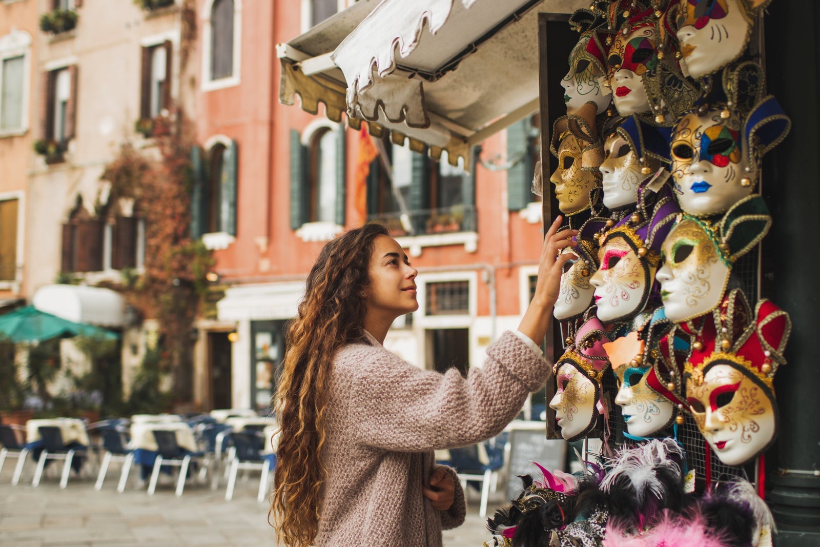 Tourist woman choosing Venetian mask on street stall in Italy.