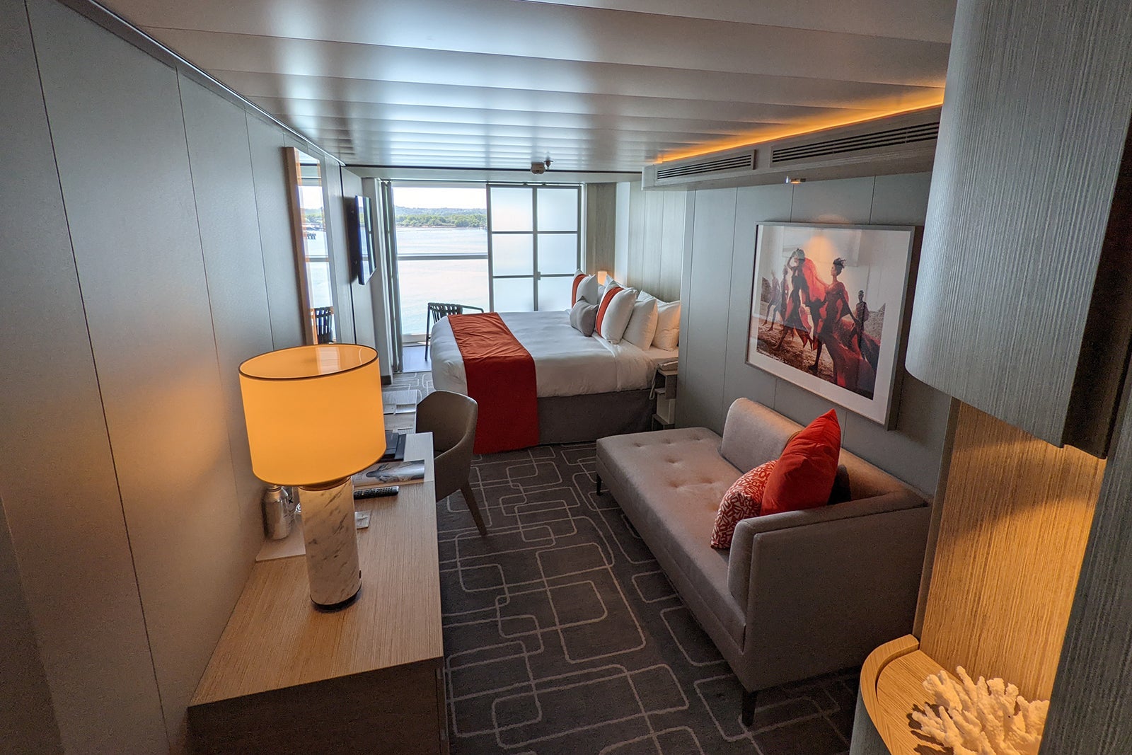 AquaClass cabin on Celebrity Beyond, showing neutral couch and bed with red accent colors.