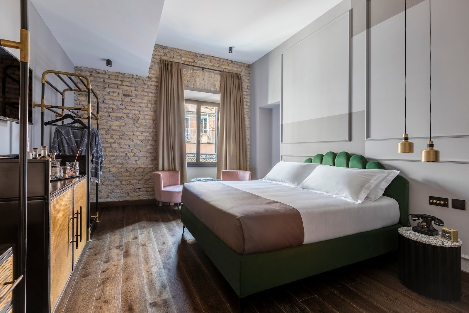 large hotel room with bed, green headboard, velvet pink chairs and wooden floor