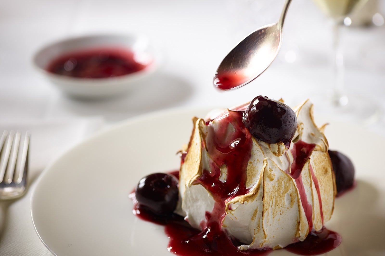 Baked Alaska with cherry sauce on white plate with spoon about to dig in