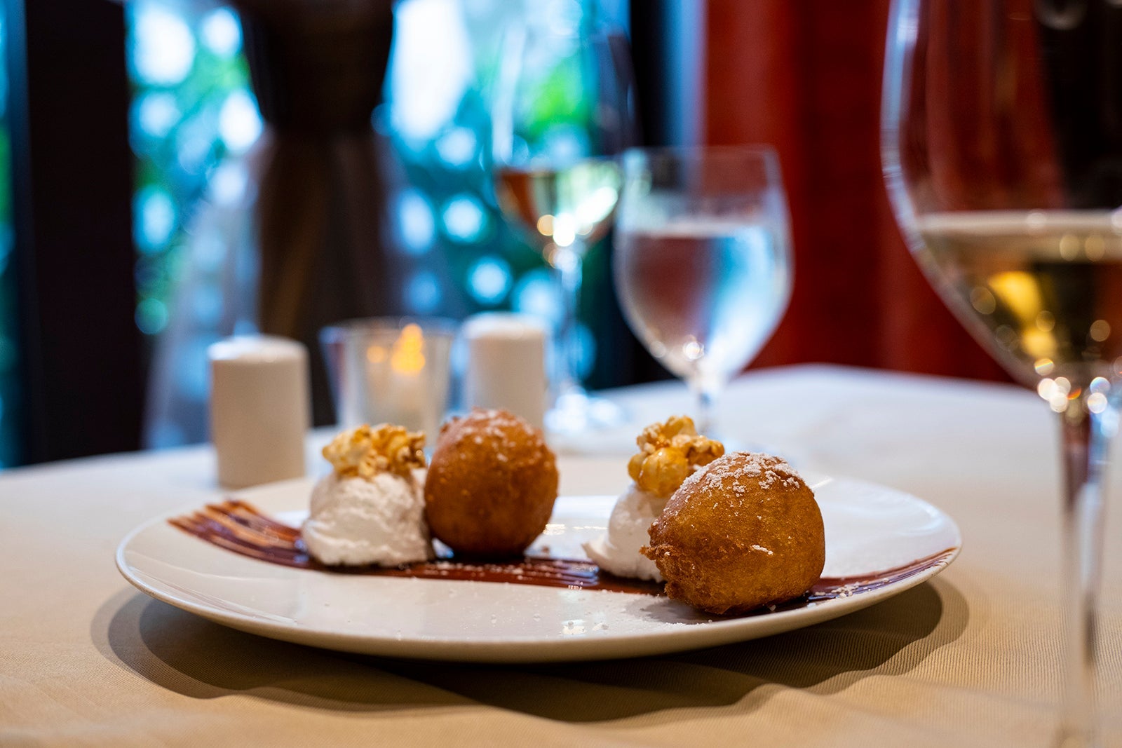 Fried cheesecake balls on a white plate with a glass of white wine