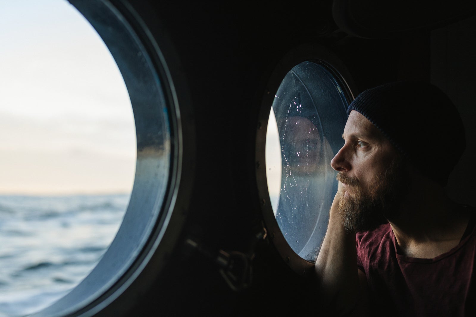 Man at the porthole window of a vessel sailing the sea, watching out in a pensive mood.
