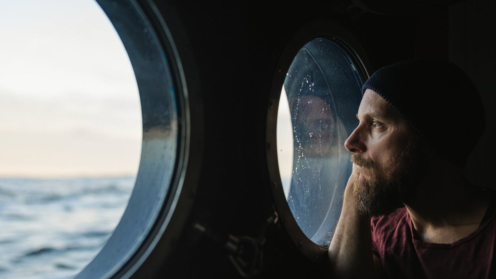 Man at the porthole window of a vessel sailing the ocean