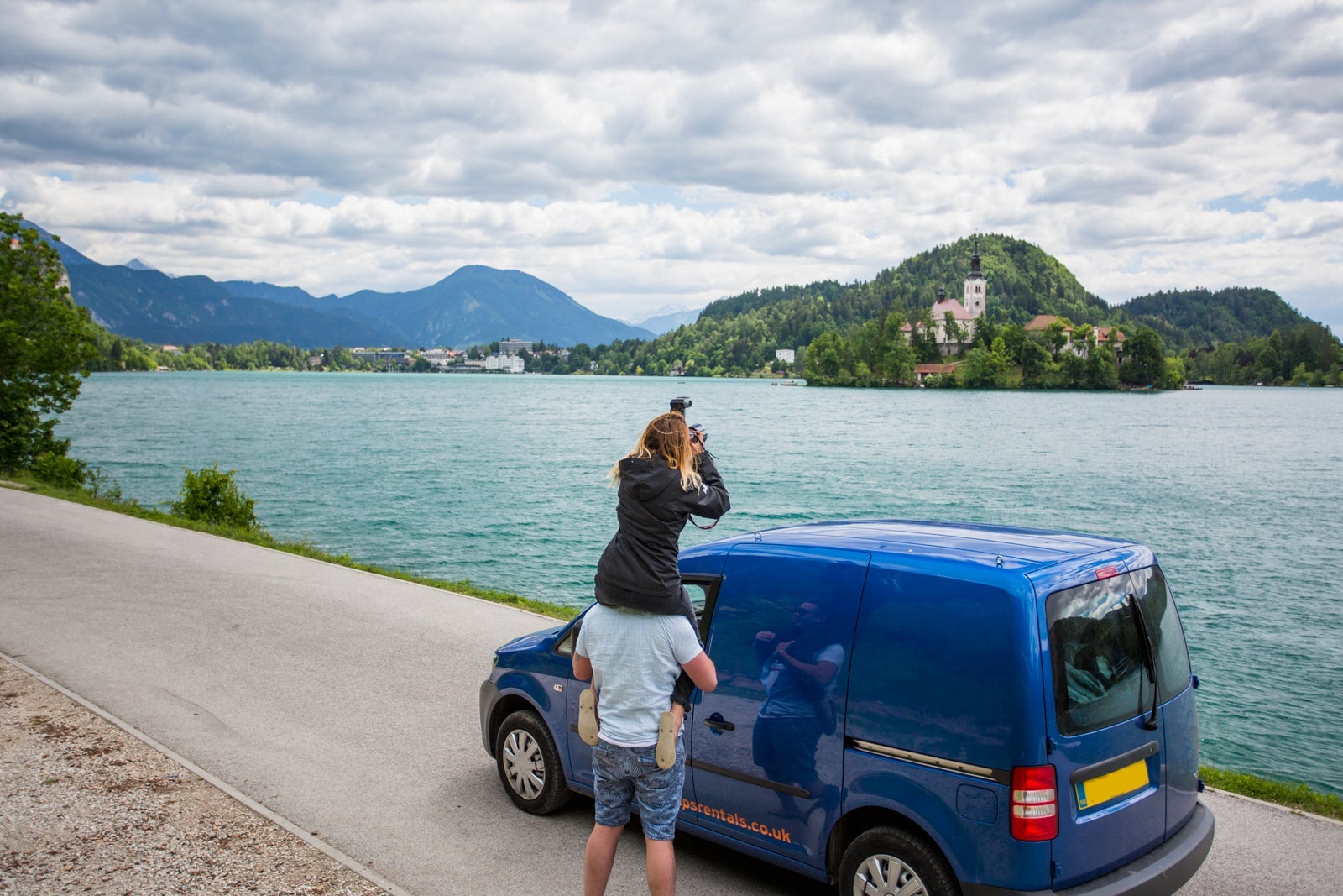 Two people stop a car to take a picture of The Church on the Island (The Church of the Assumption) in Bled, Slovakia.