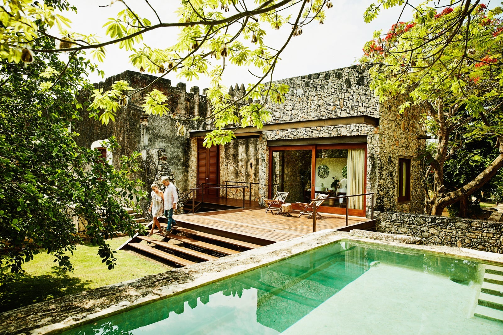 Senior couple holding hands and walking down steps outside of bungalow at luxury tropical resort