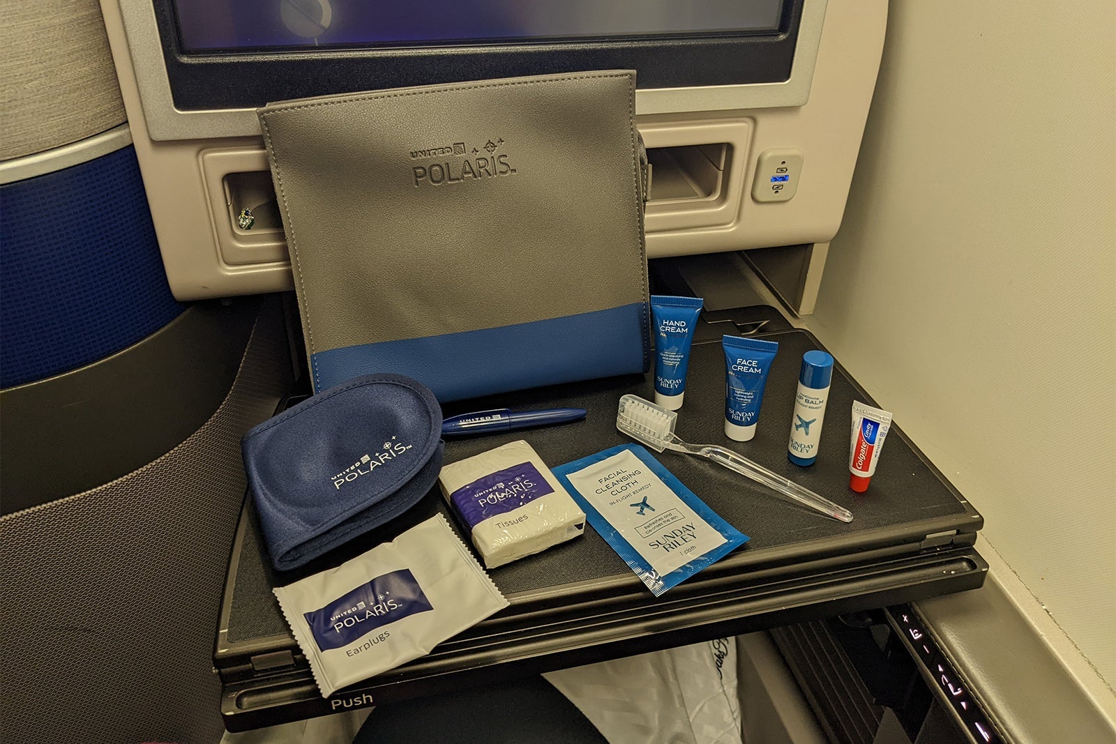 Airplane tray table with amenity kit featuring toothbrush, socks, eye mask and lotion bottles