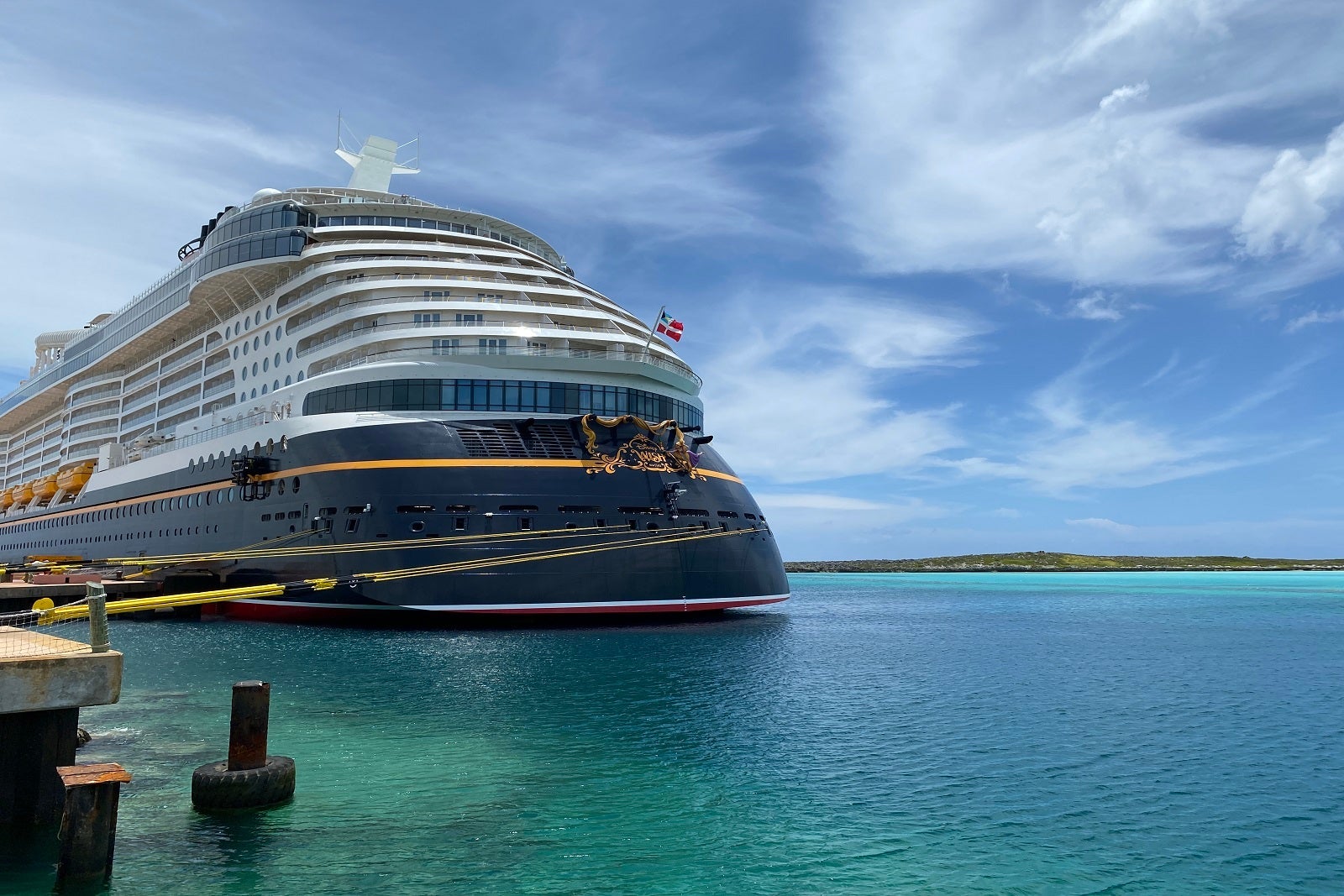 The aft of a docked cruise ship, tied up and floating on teal water