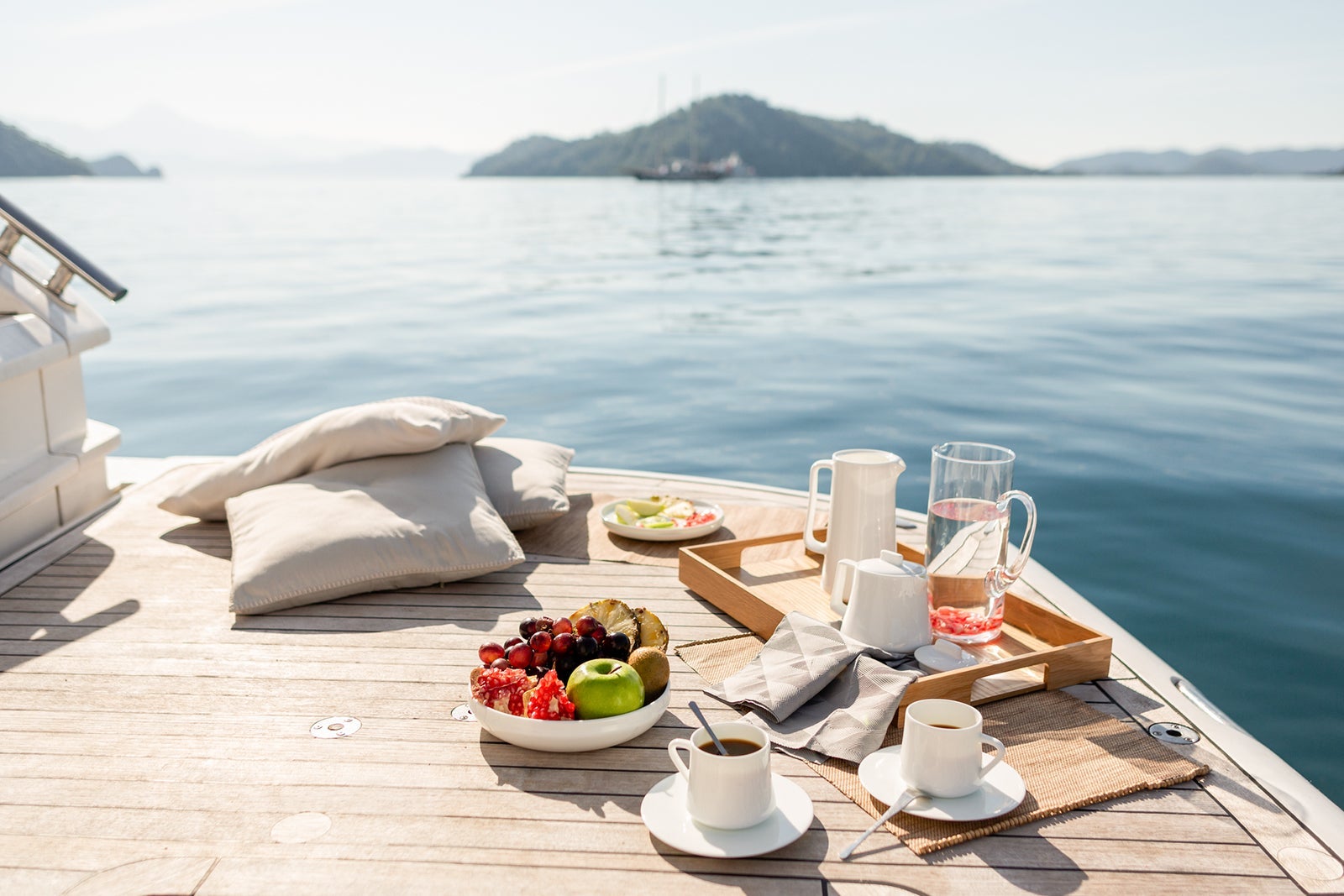 A breakfast tray with drinks and fruit sitting on the deck of a ship facing the water