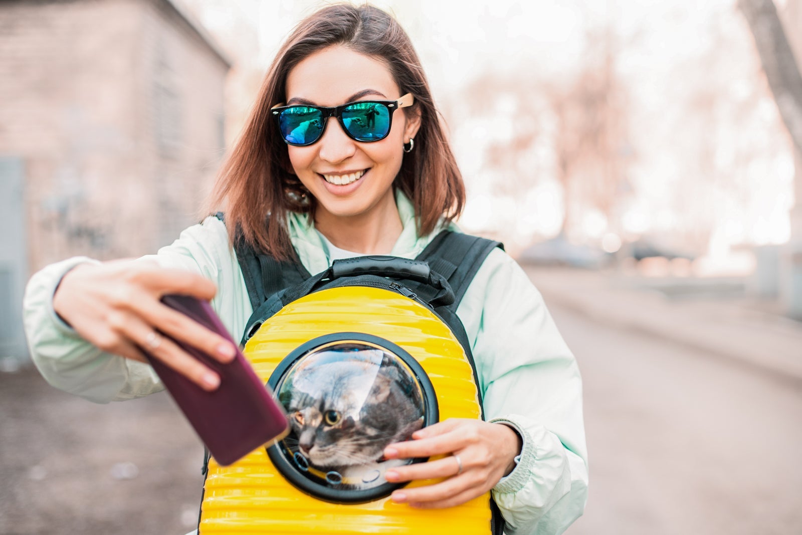 Happy Girl pet owner smiles in the Park walking with her cat. She taking selfie photo for her blog or social media. Friendship and cat carrier concept