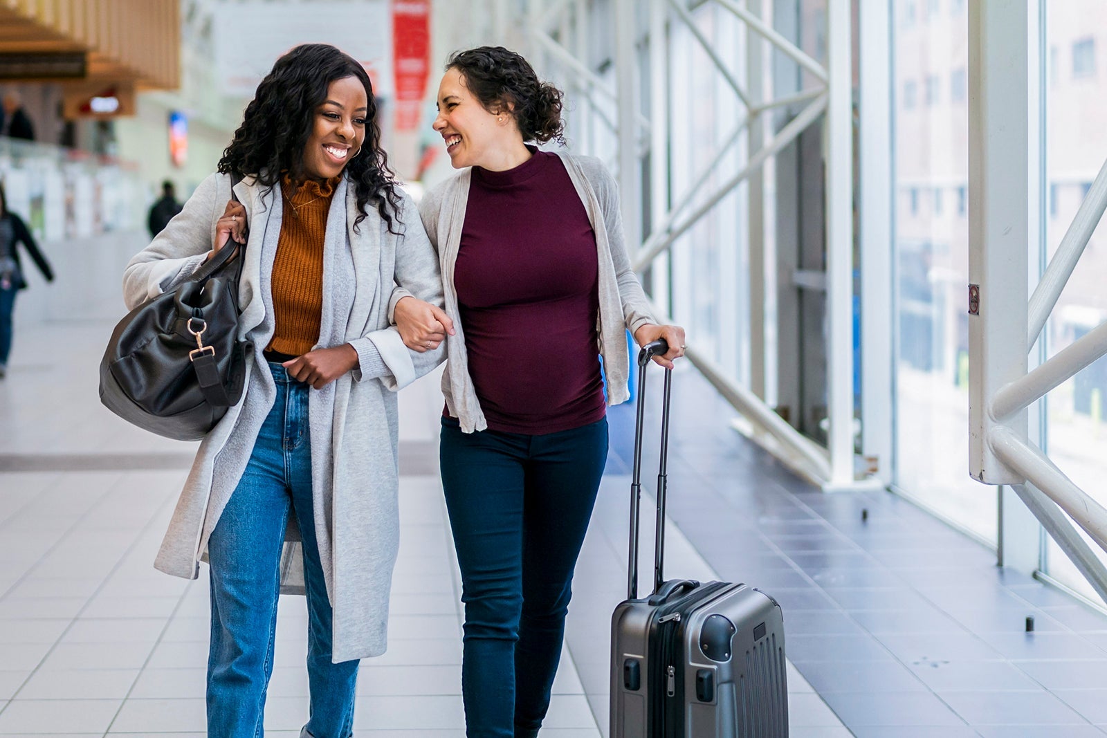 friends walk arm-in-arm through an airport while laughing