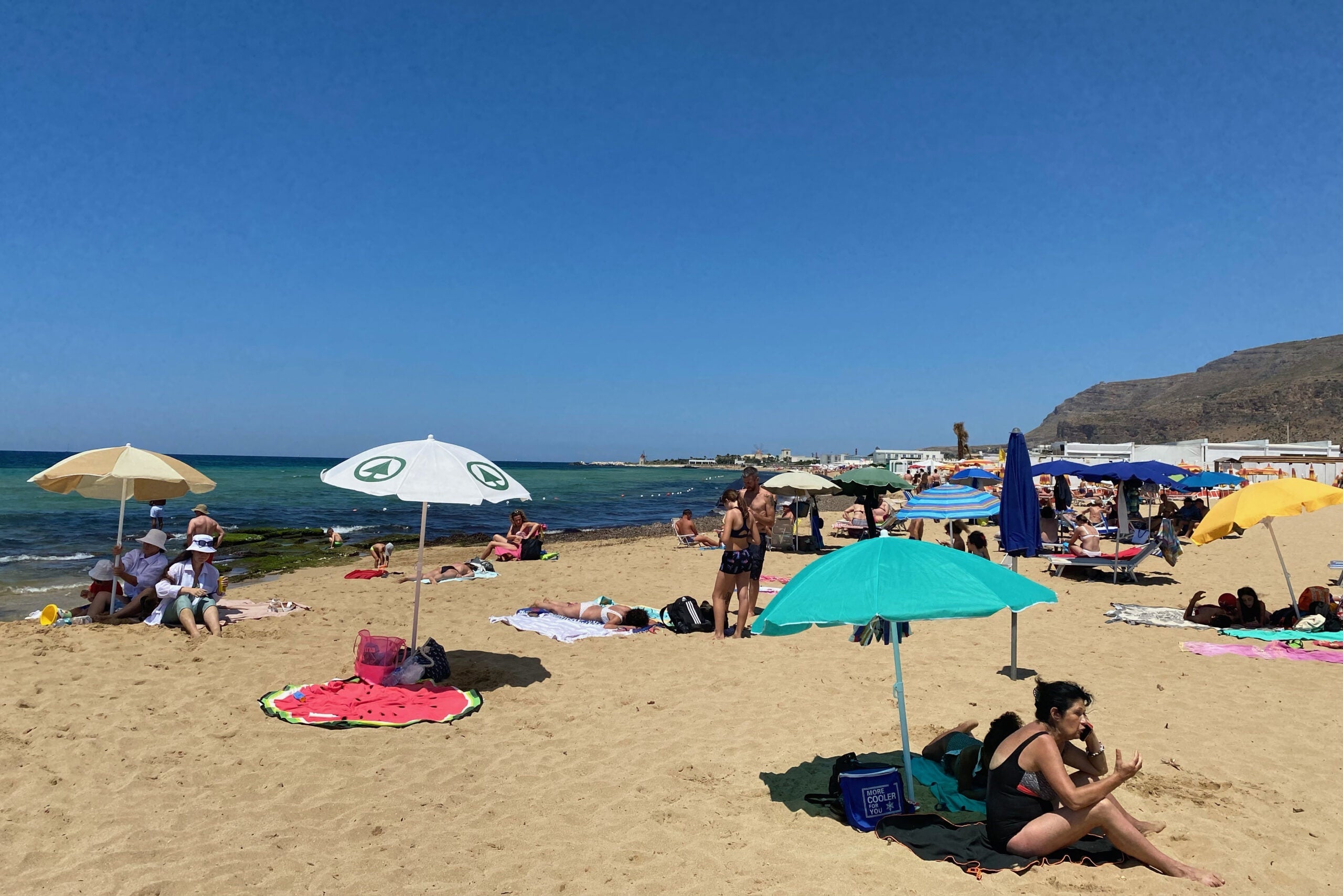 Sunbathers and colorful umbrellas on San Giuliano Beach, Trapani, Italy.