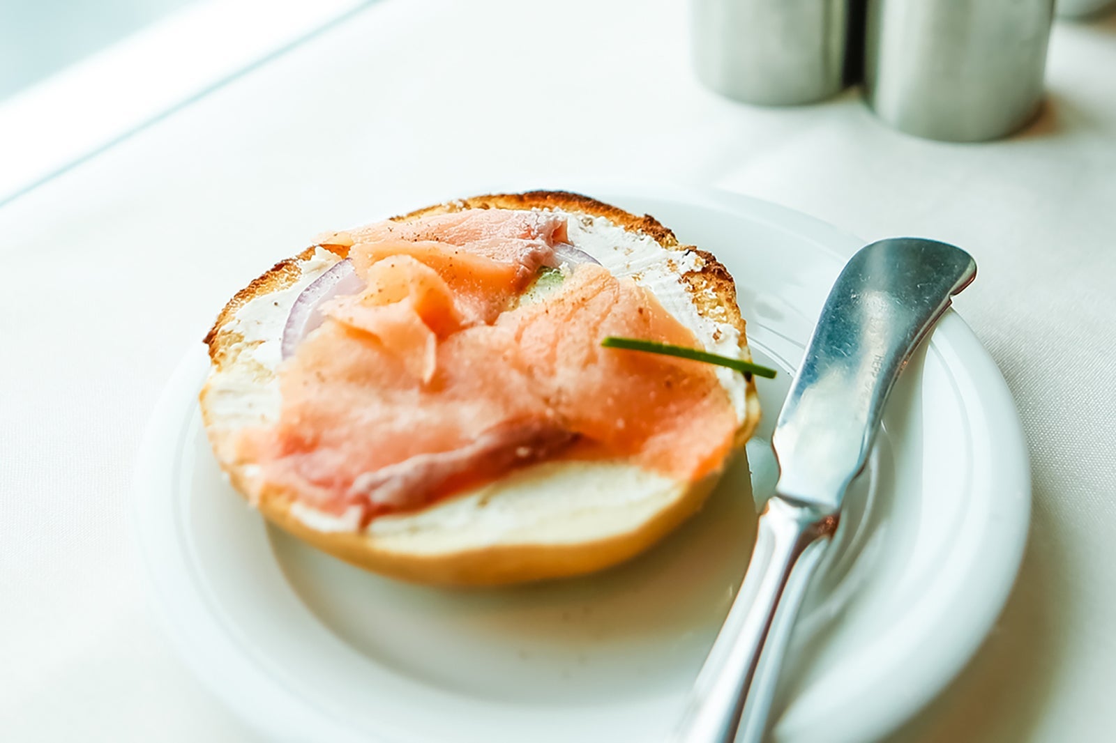 Sliced fish on a bagel on a white plate with a butter knife next to it