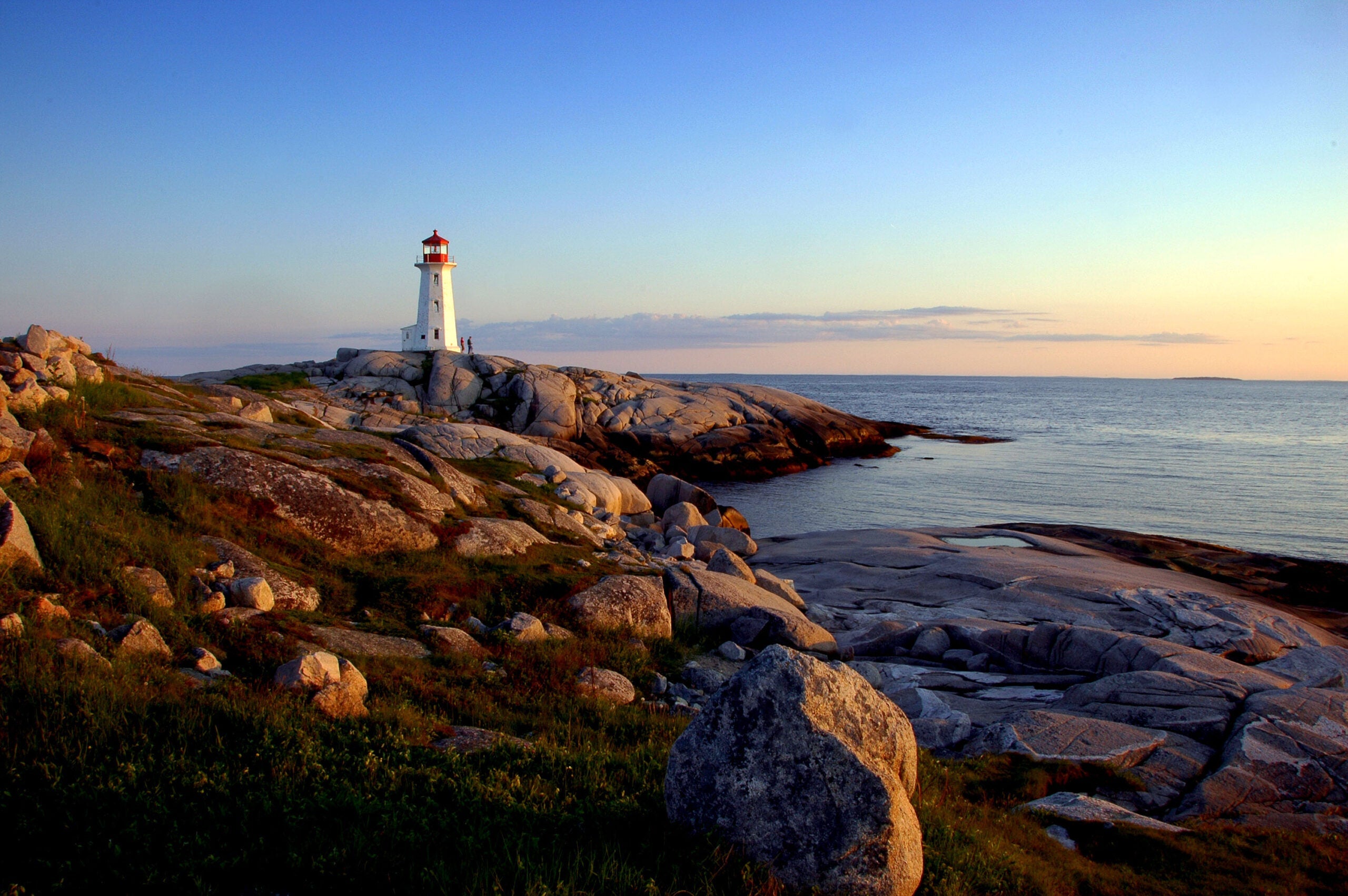 A white and red lighthouse on a rock outcropping overlooking the sea in Nova Scotia, Canada