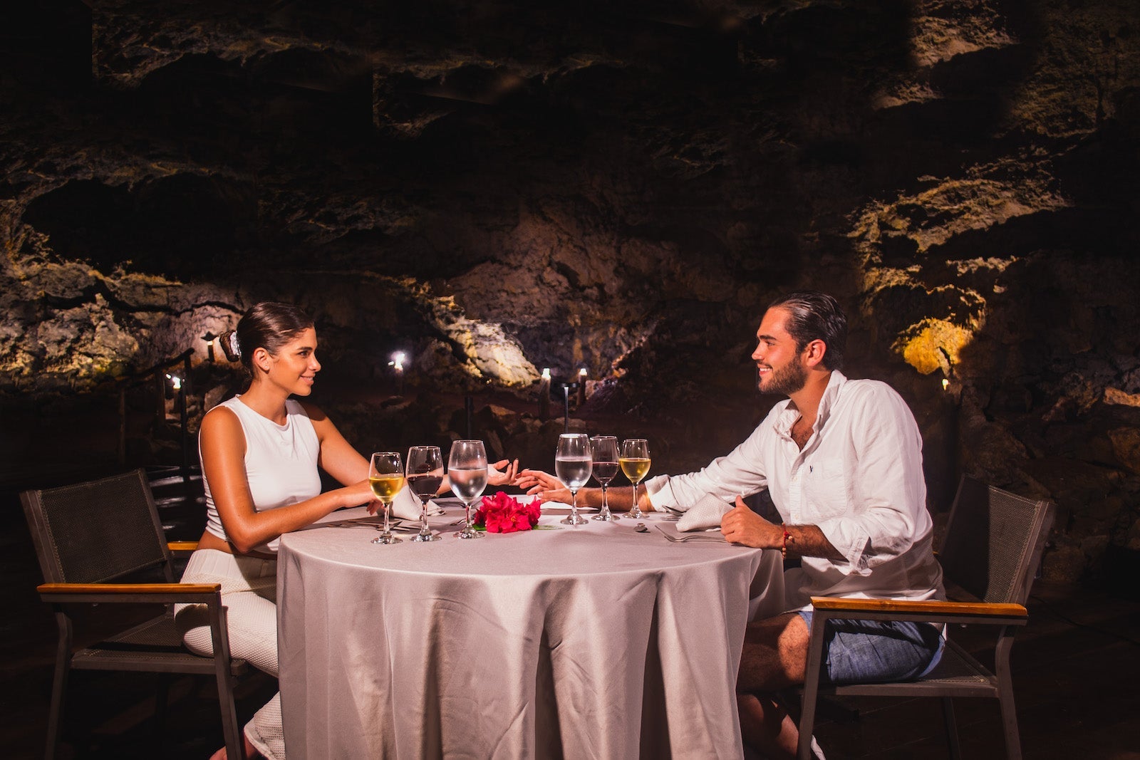 Couple sitting at dinner table in cave holding hands, drinking wine