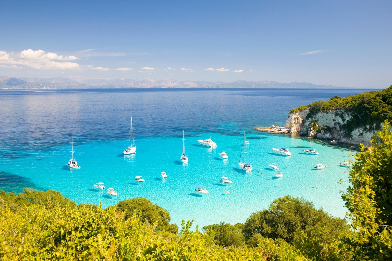 An island inlet of crystal blue water filled with white sailboats and surrounded by green vegetation