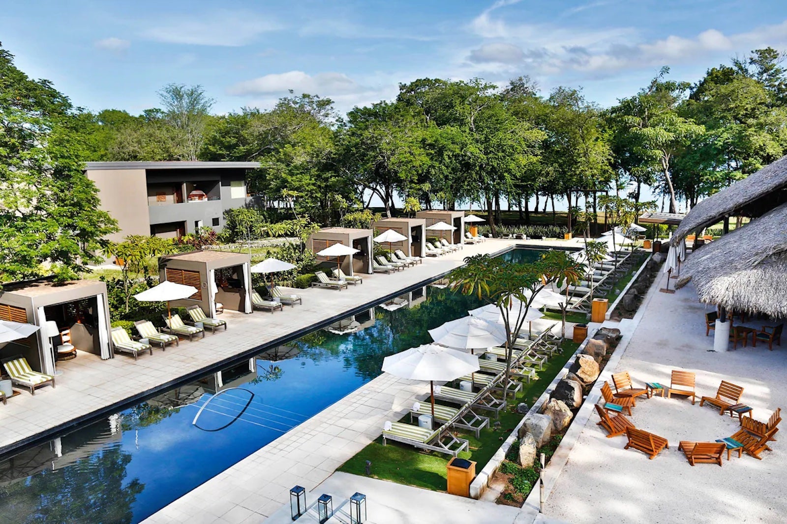 view of long reflecting pool surrounded by pool chairs, green trees are in the distance
