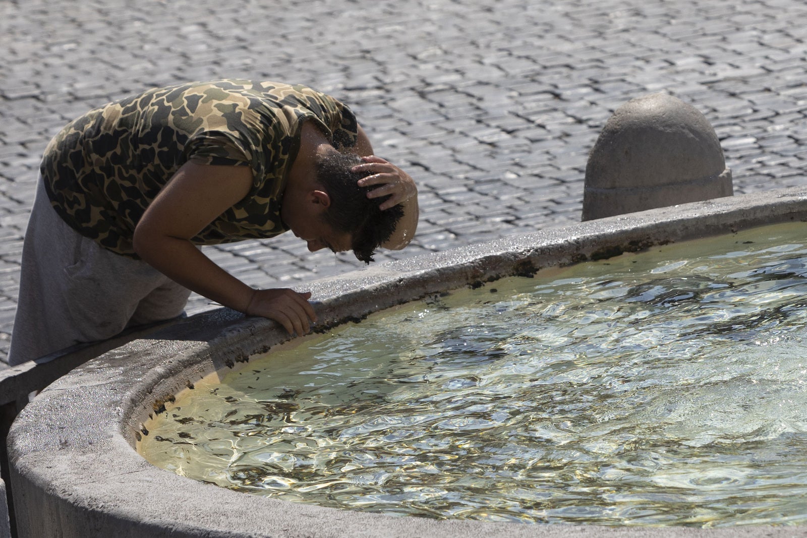 A tourist refreshes himself at a fountain in Piazza del Popolo in Rome