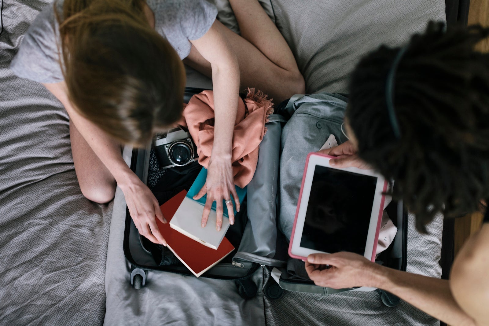 Interracial couple packing suitcase, with tablet computer, books, cloths, and 35mm camera.