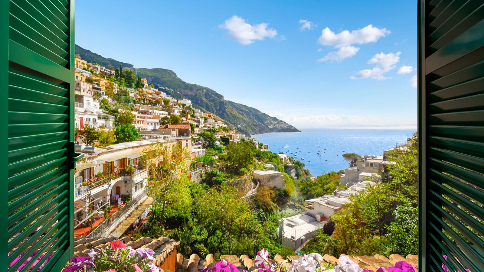 Mountain, city and sea view through an open window with shutters of the city of Positano on the Amalfi Coast of Southern Italy during summer.