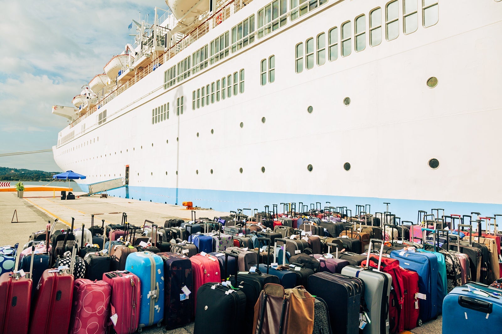 Dozens of suitcases sitting in rows on a pier next to a cruise ship