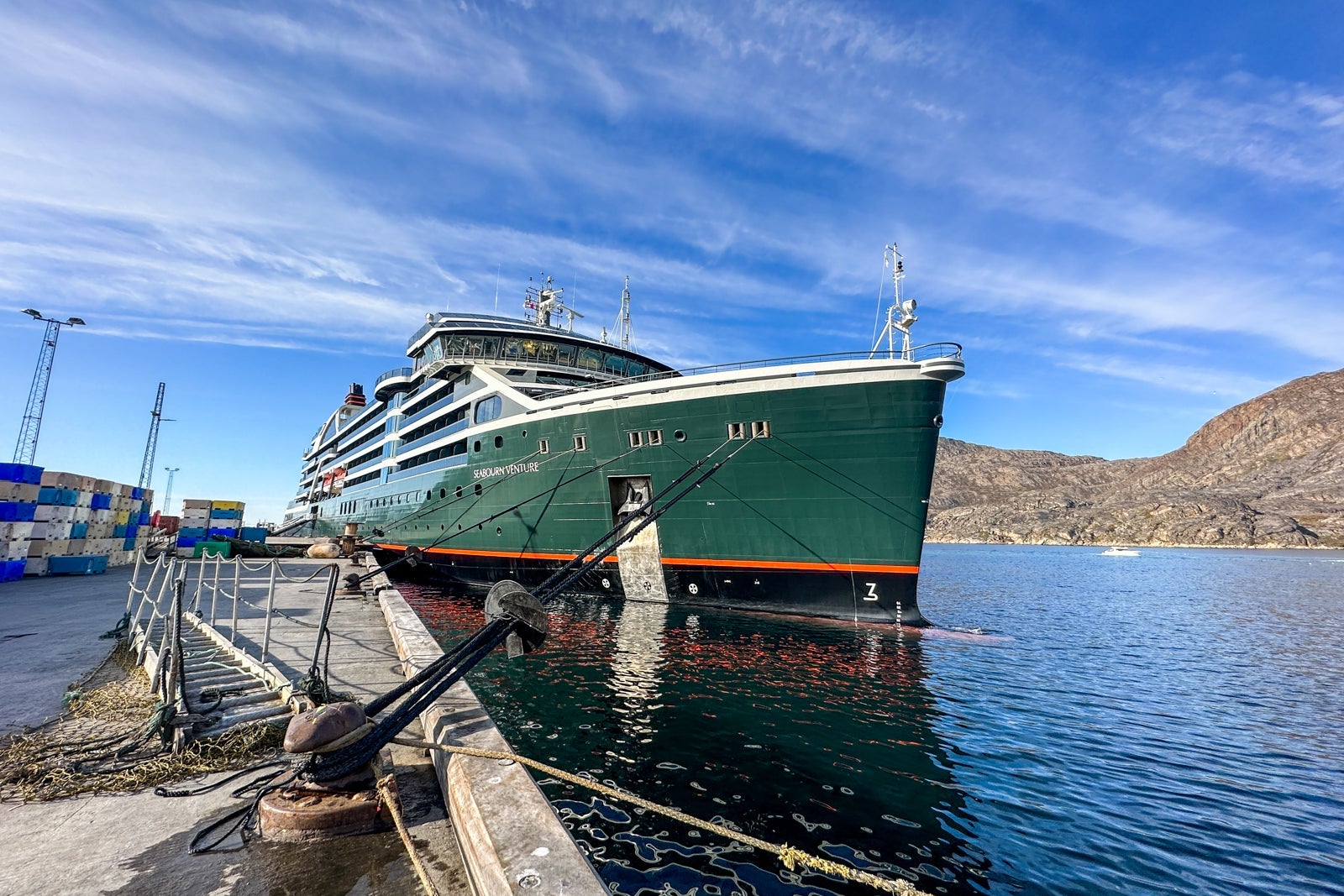 A green-hulled cruise ship docked in blue water with blue sky overhead