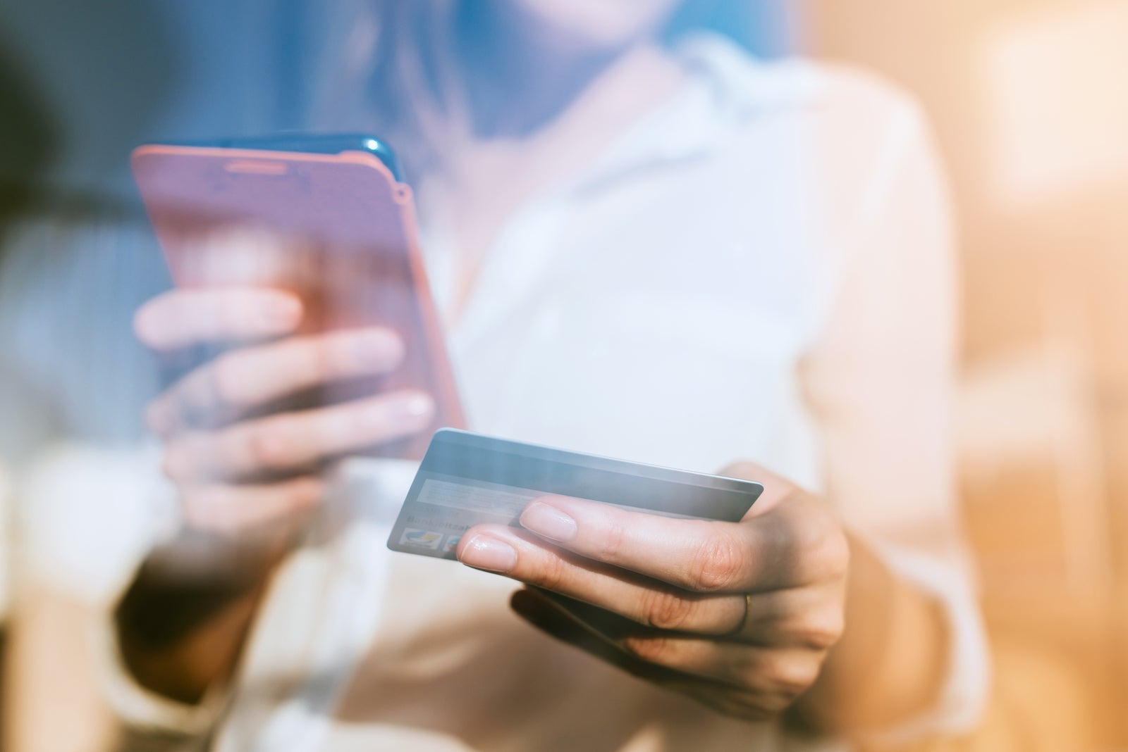 an unseen person holds a credit card and a smartphone