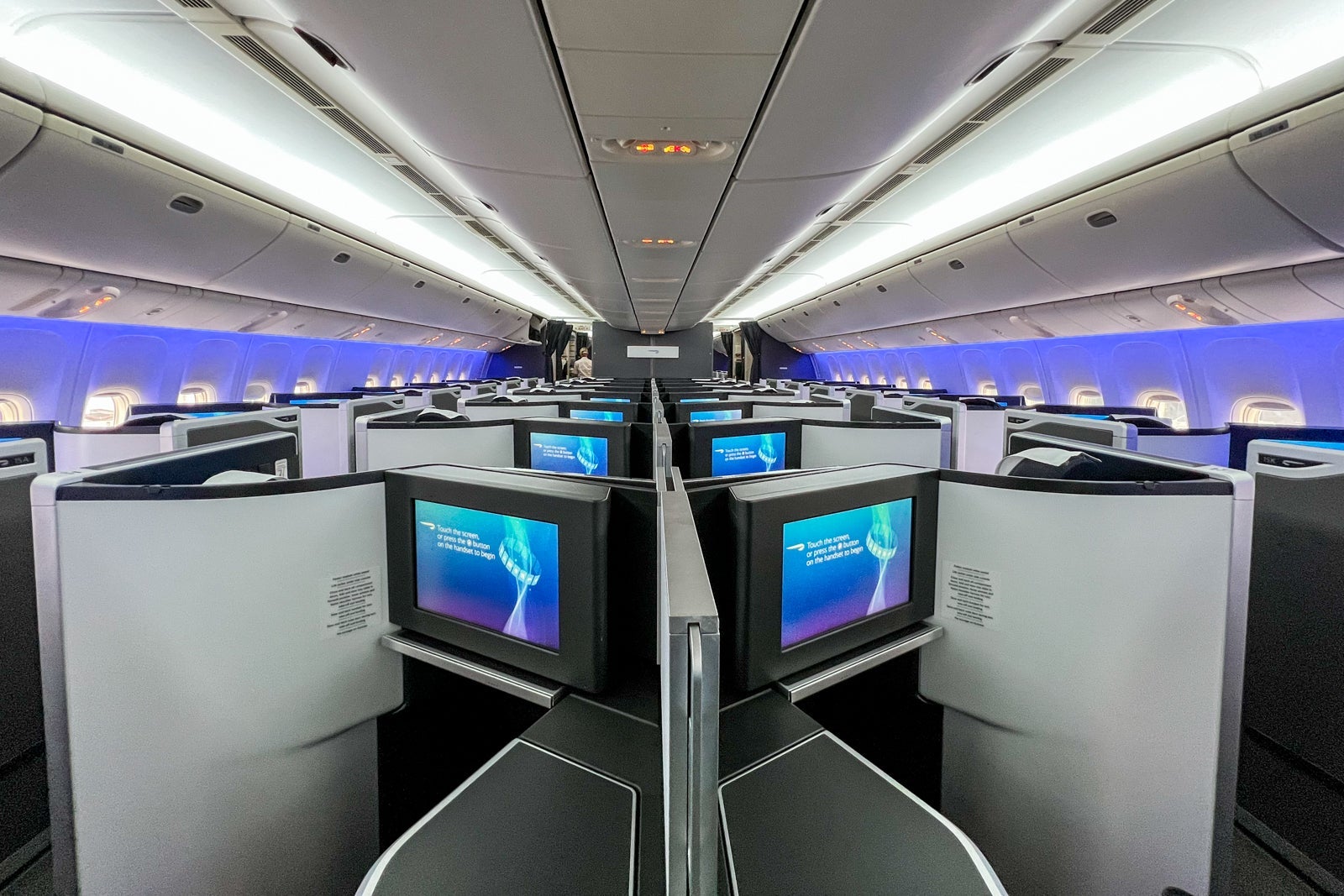 an airplane cabin with blue lighting and business-class seats divided by walls