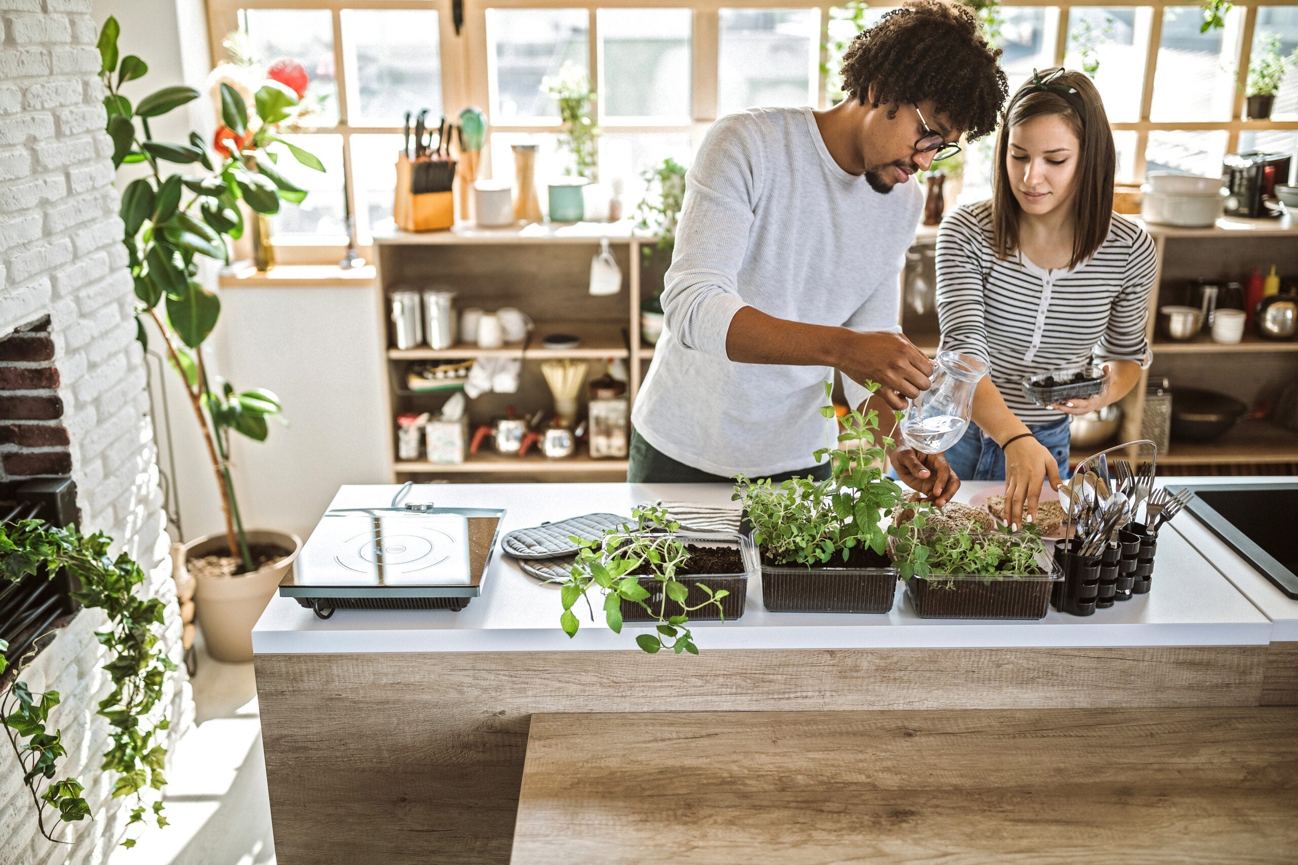 Multi-ethnic couple taking care of kitchen herbs.