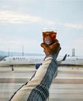 A person holding a Starbucks iced coffee in front of a Delta plane